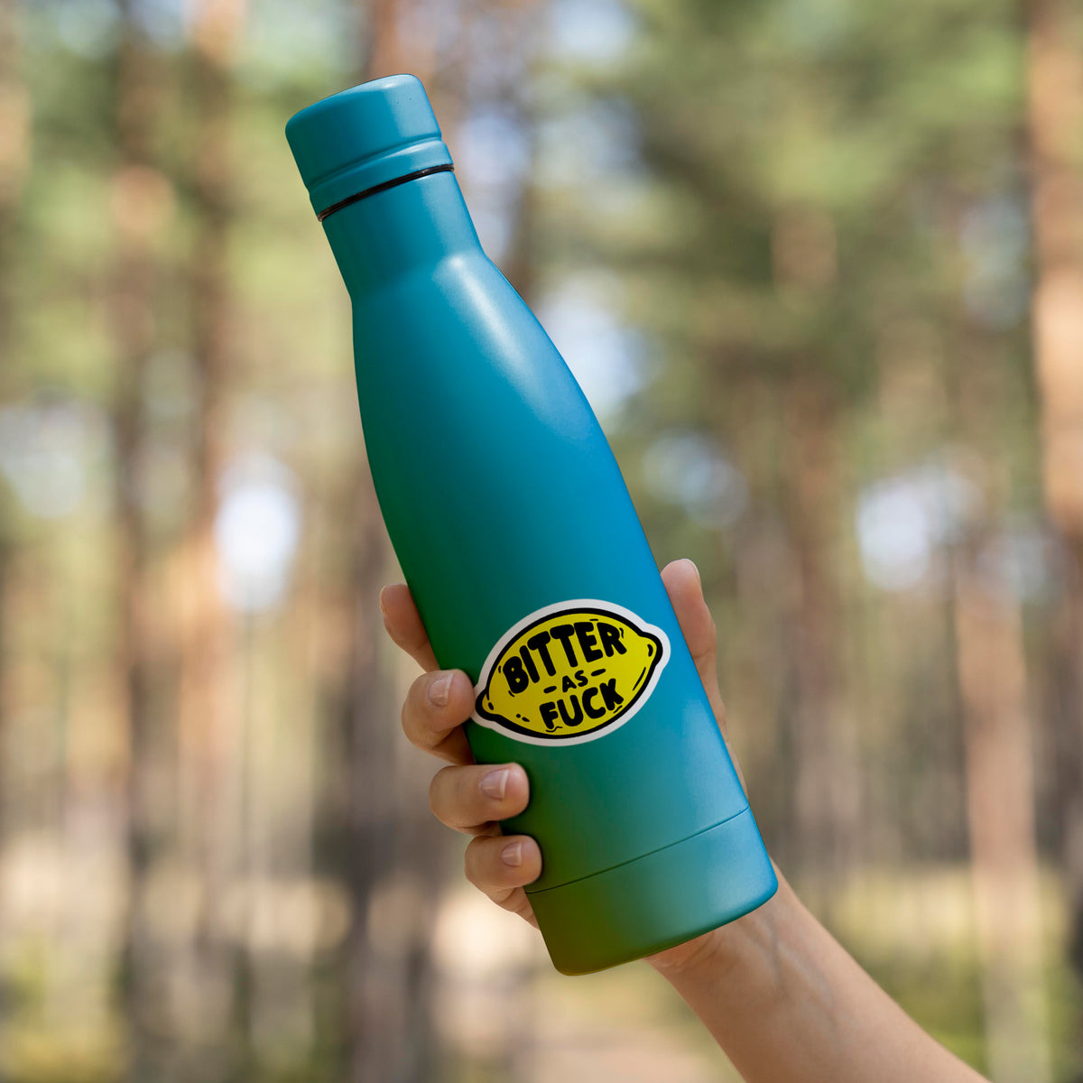 A person holding a Bitter Sticker water bottle with a blue matte finish in the woods, made by KosmicSoul.