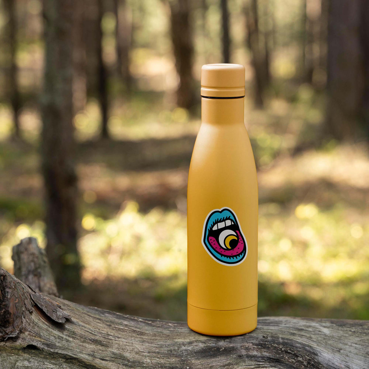 An Eye In Mouth Sticker water bottle sits on a log in the woods.
