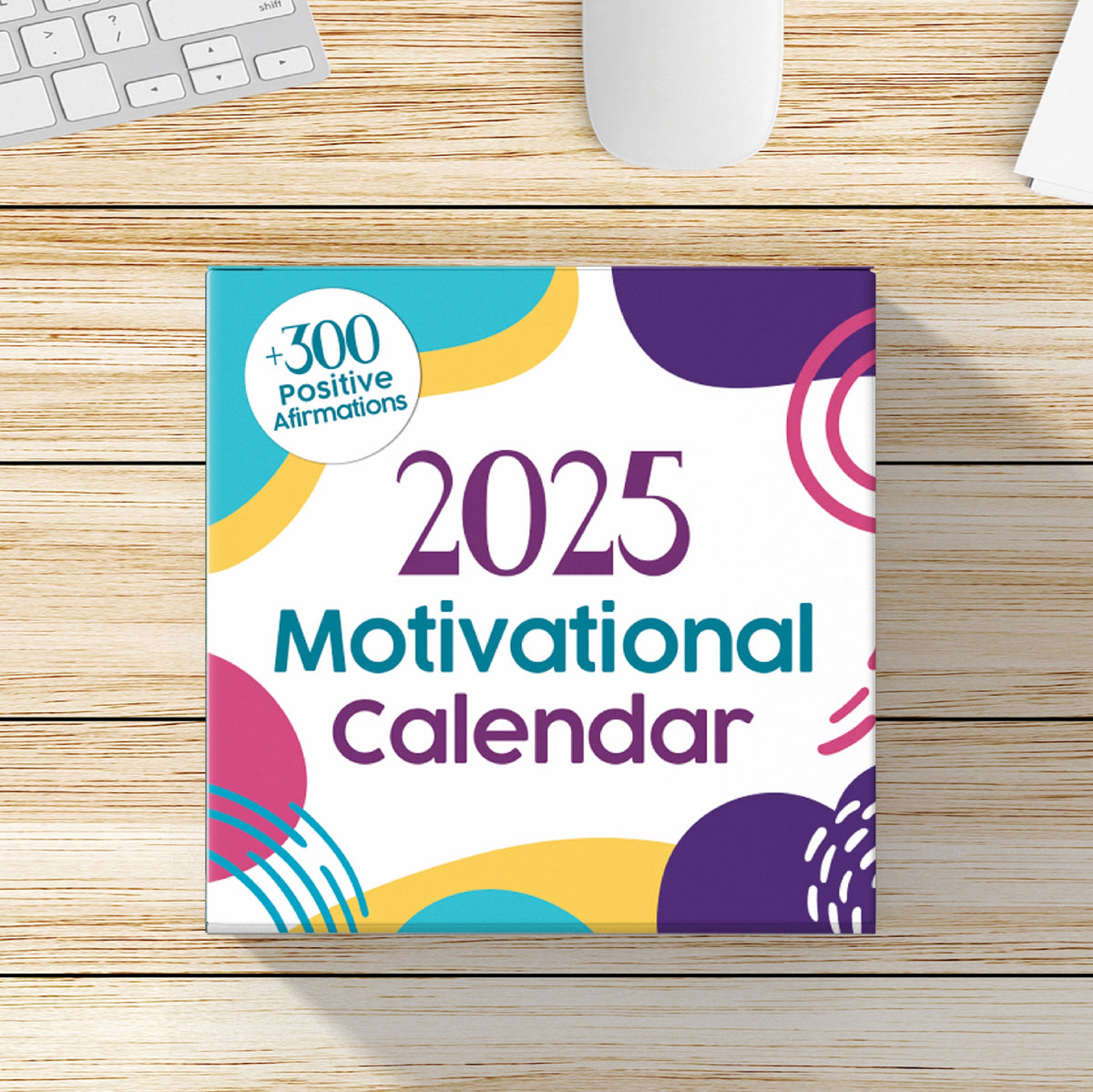 Overhead view of the Kosmic Soul 2025 Motivational Calendar, featuring vibrant designs and a label highlighting its collection of over 300 motivational quotes, laid on a wooden surface beside a keyboard and mouse—perfect for enhancing any desk or tabletop setting.