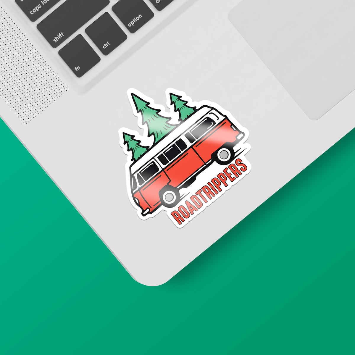 A laptop with a matte finish and a KosmicSoul Roadtrippers sticker of a red van with trees on it.