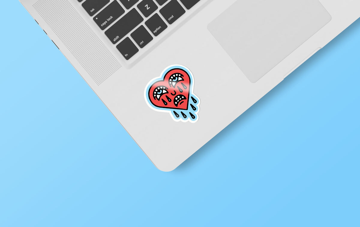 A laptop with a Crying Heart sticker from KosmicSoul on it, featuring a matte finish and compact dimensions measuring max 4&quot;.